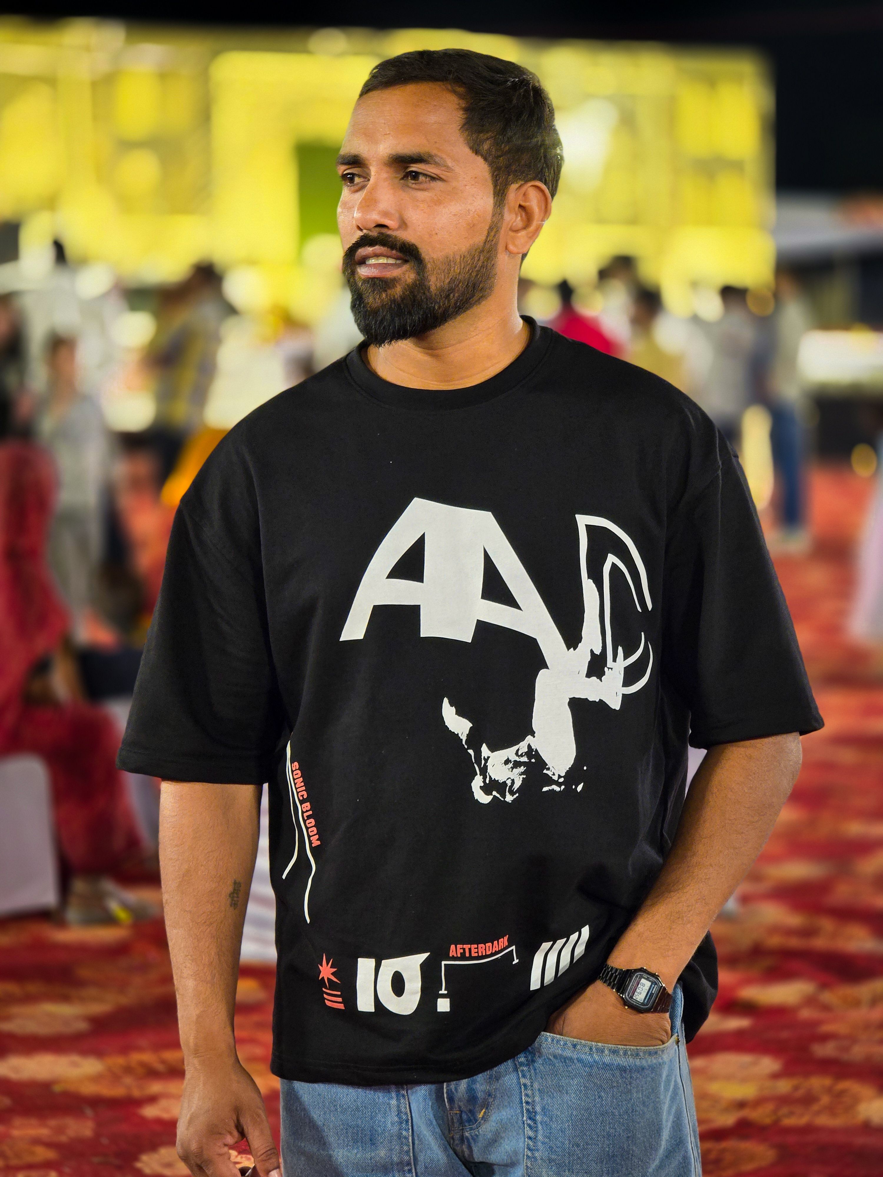 Man in casual black T-shirt at vibrant outdoor event with blurred crowd.