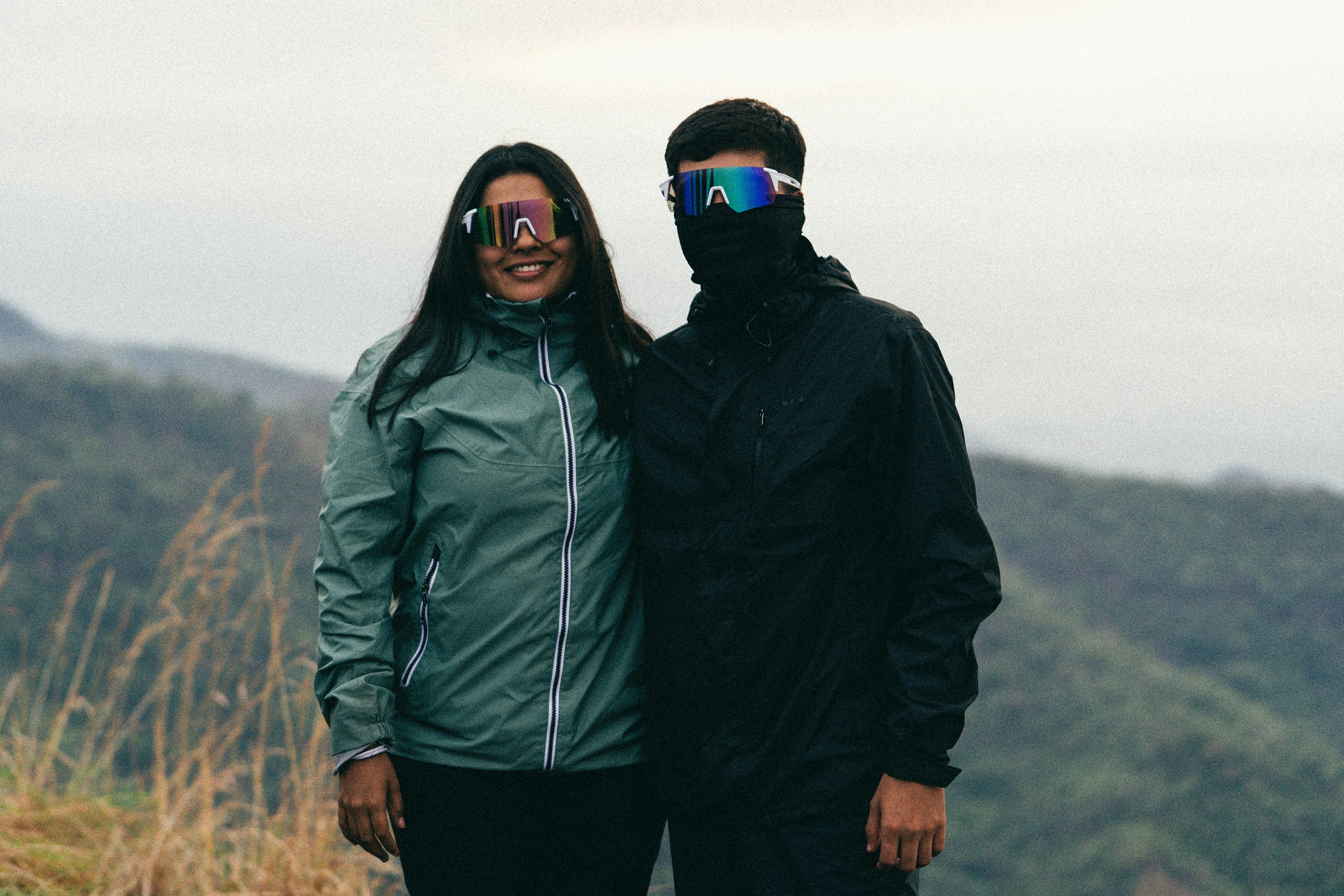 A couple wearing sunglasses and sporty jackets enjoying a scenic outdoor view.