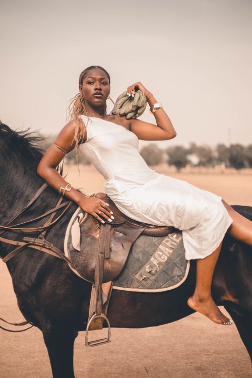 Free Stylish woman in white dress confidently poses on a black horse in a serene outdoor setting. Stock Photo