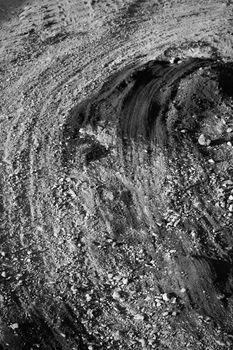 Monochrome image of tire tracks in gravel, showing texture and patterns.
