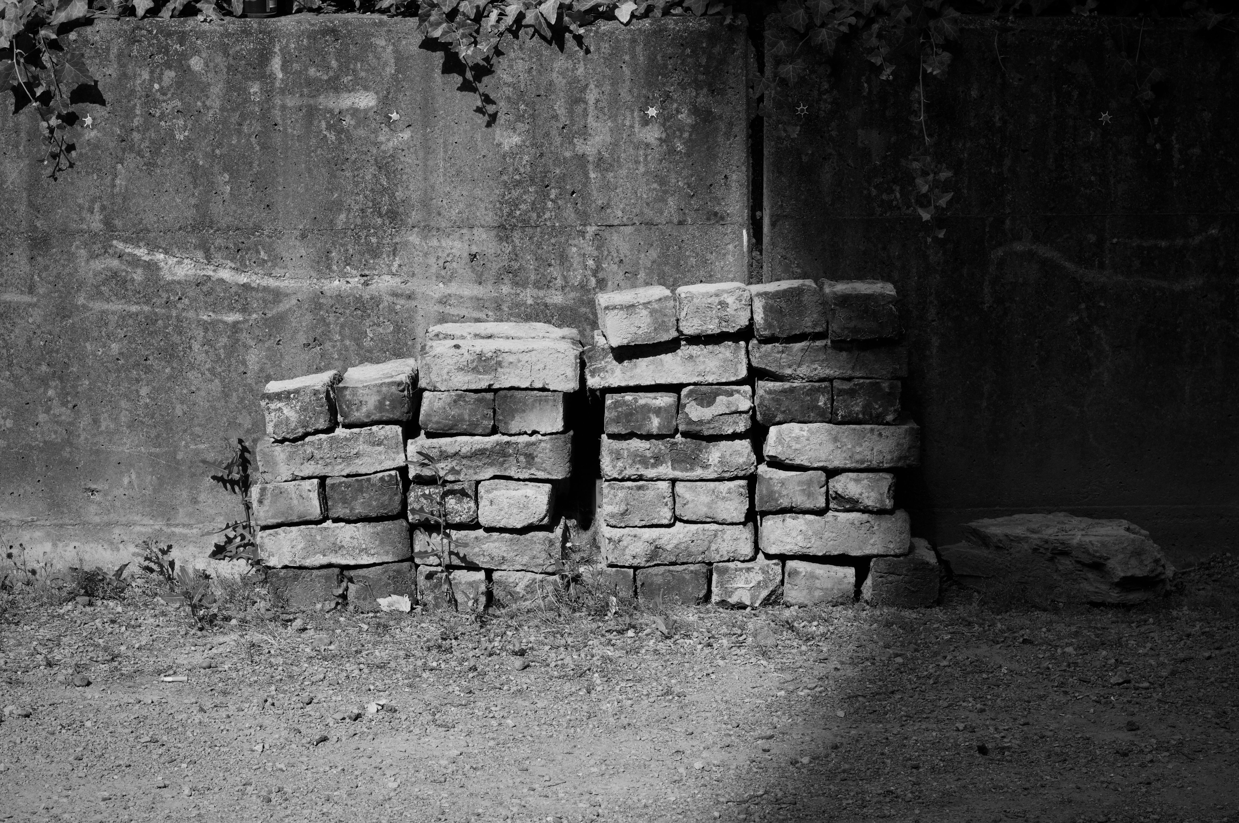 Black and white photo of stacked bricks next to a concrete wall.