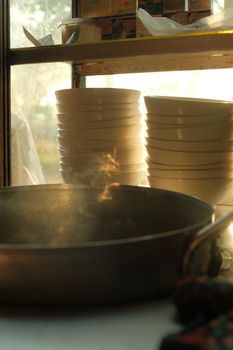 Steaming pot with stacked bowls in a traditional Vietnamese kitchen setting, lit by warm natural light.