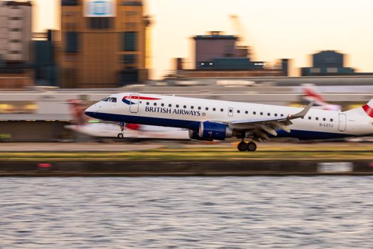A British Airways airplane descends at an urban airport during sunset, showcasing motion and urban landscape.