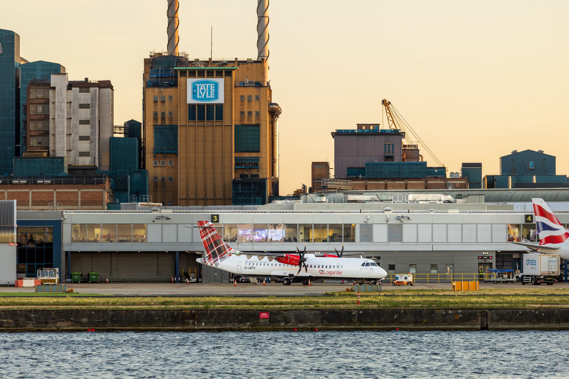 View of airplanes parked at London City Airport with industrial buildings in the background at sunset.