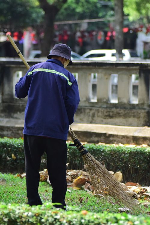Free Elderly man in blue sweeping leaves in an urban park setting outdoors. Stock Photo