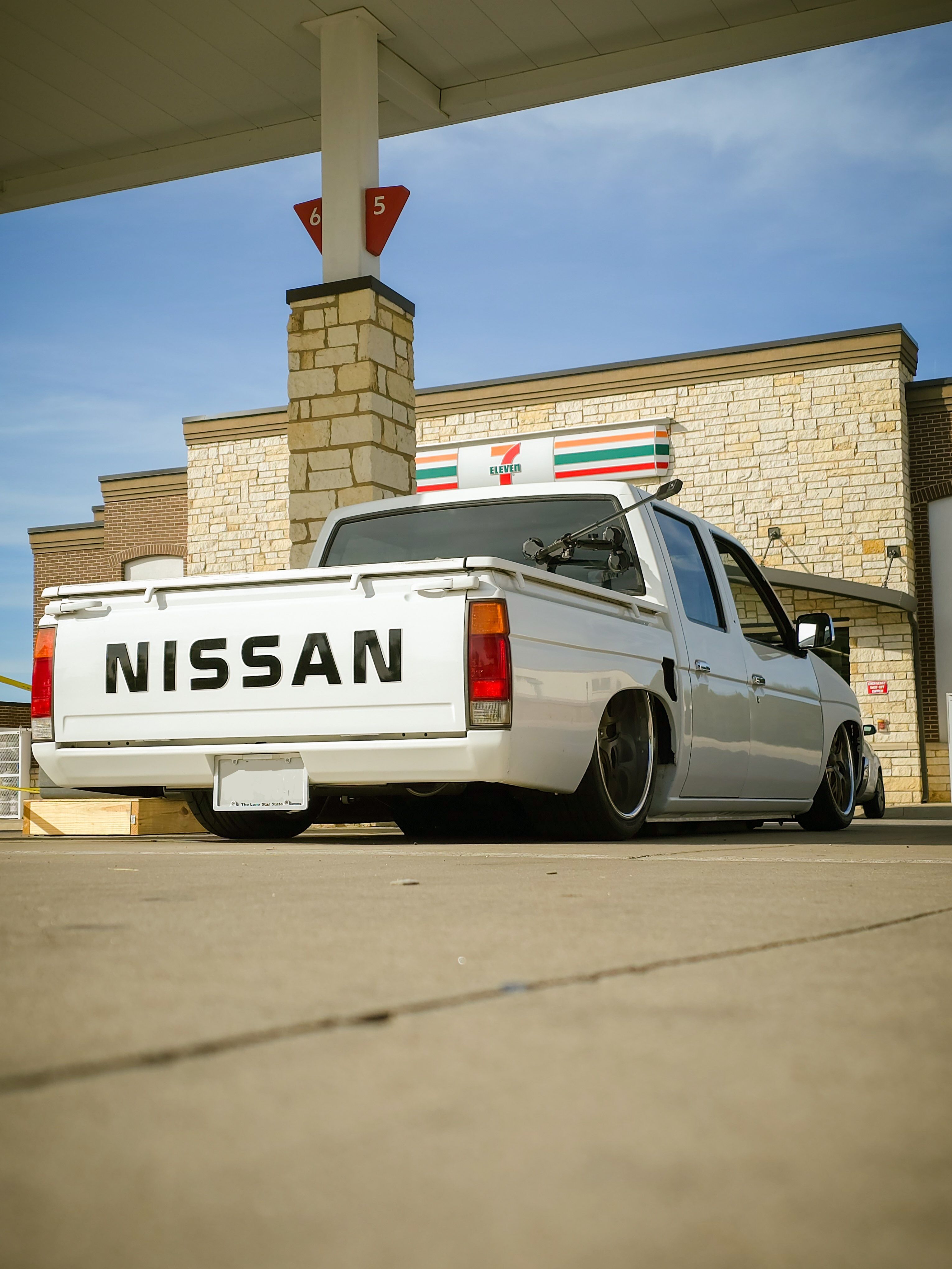 A modified white Nissan pickup at a gas station, showcasing a lowered suspension and urban setup.