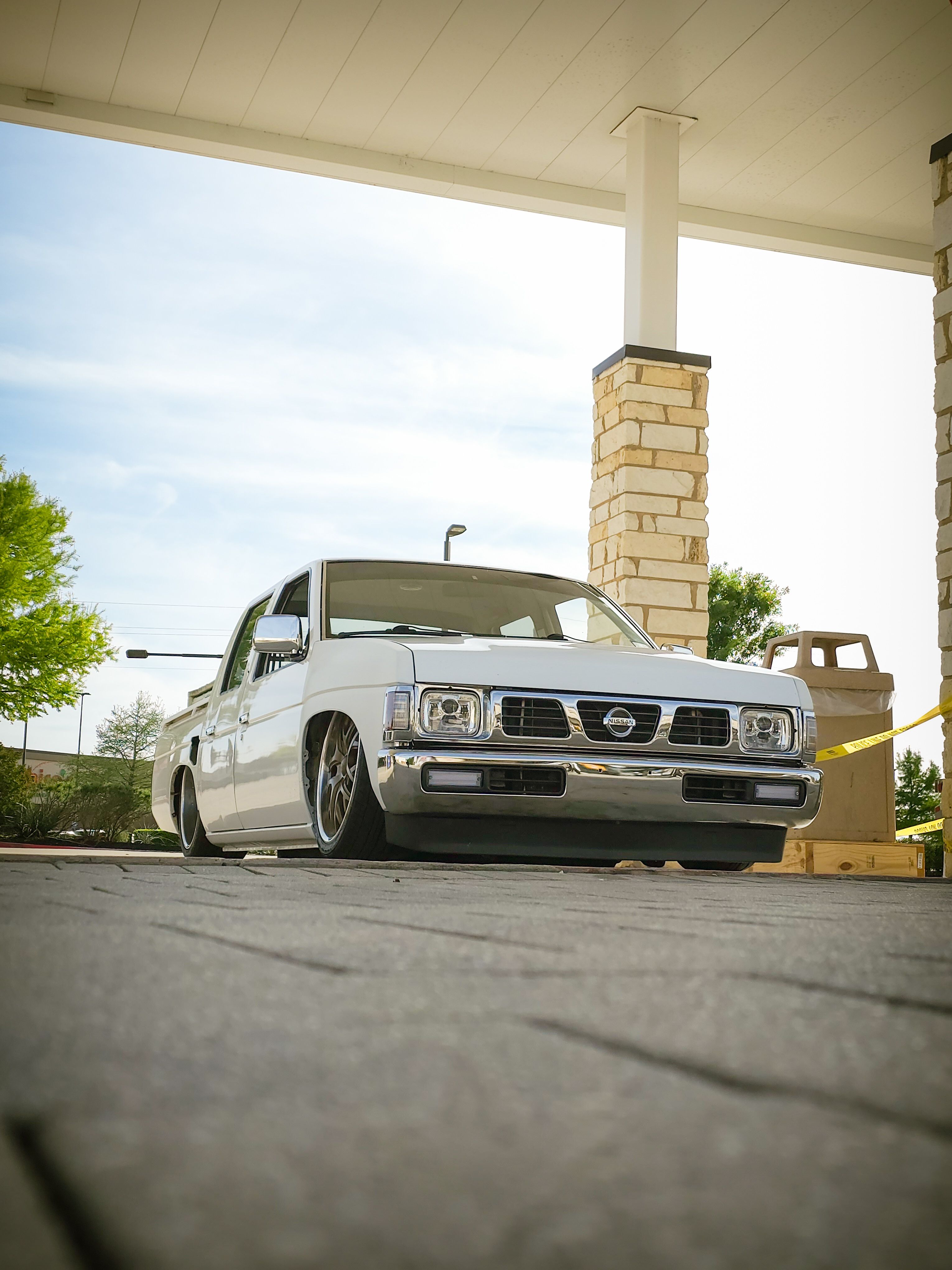 Low angle view of a vintage white Nissan pickup truck parked at a gas station.