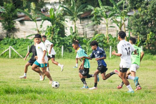 Young boys playing an intense soccer match on a grassy field in Myawaddy, Myanmar.