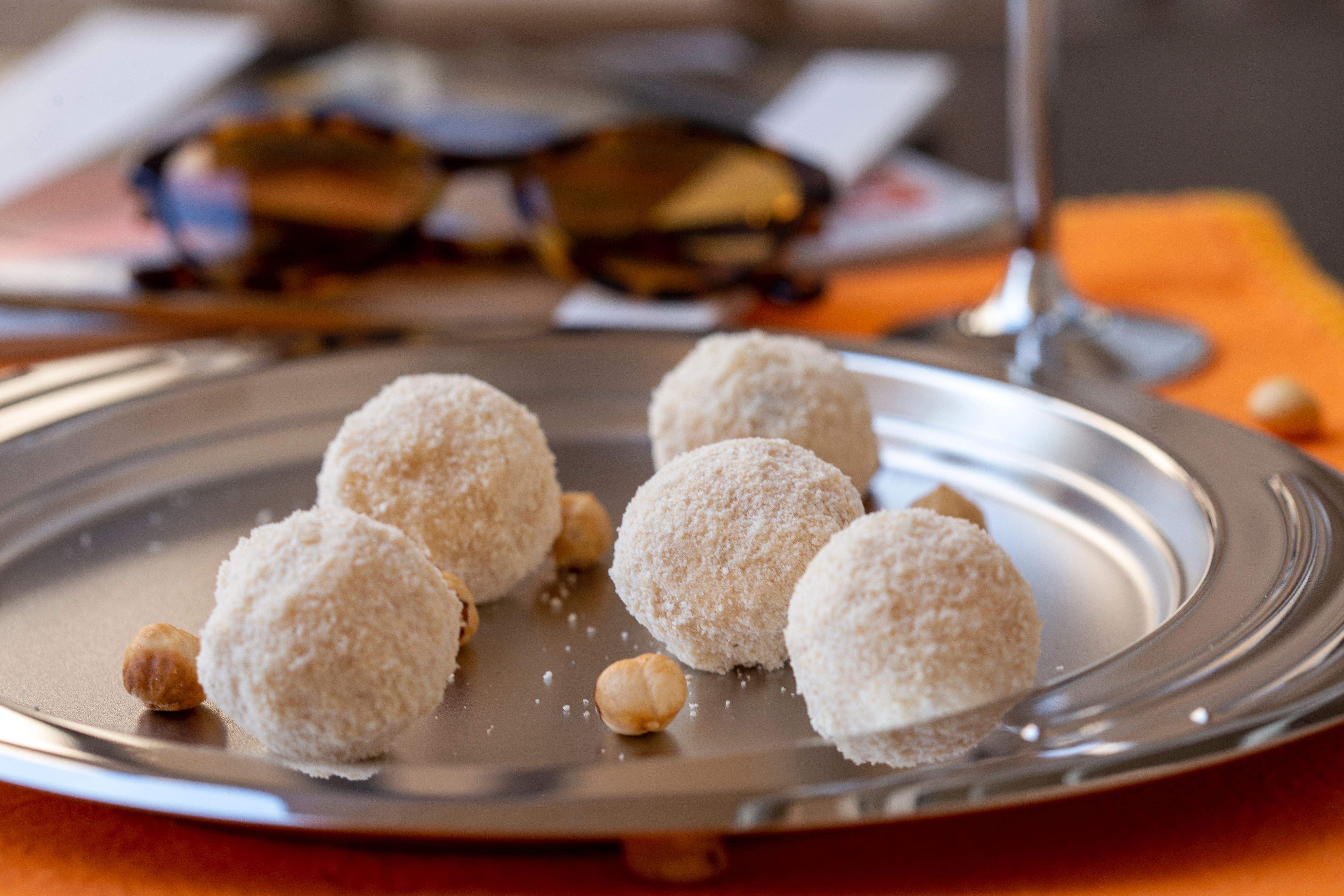 Close-up of white coconut truffles and hazelnuts on a silver plate.