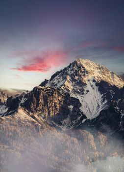 Stunning view of a snow-capped mountain with vibrant sunset hues and low clouds.