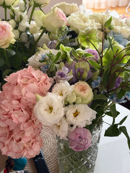 Free Close-up of a colorful bouquet featuring roses, hydrangeas, and lisianthus in a glass vase. Stock Photo