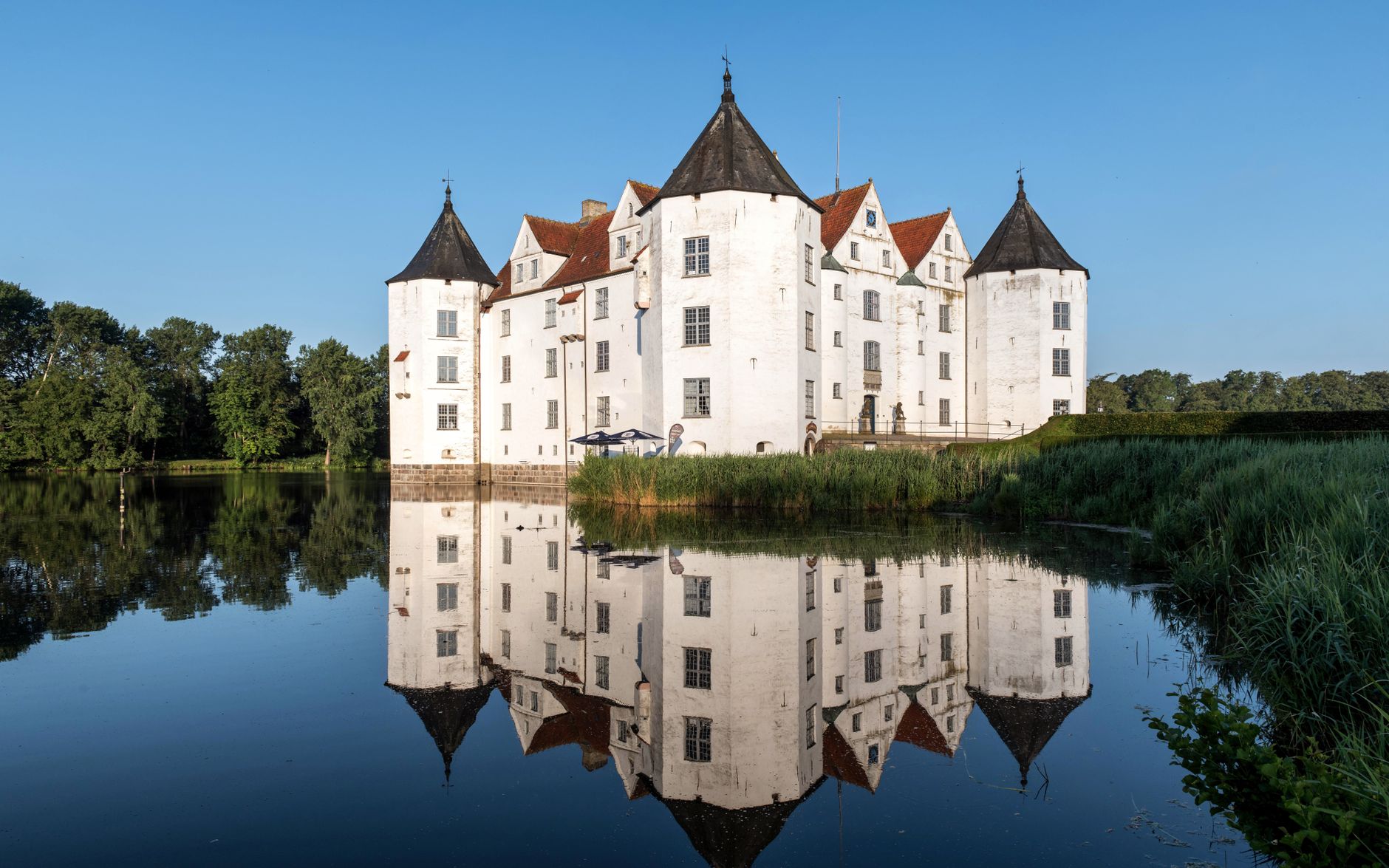 Reflective view of Glücksburg Castle surrounded by serene summer landscape.