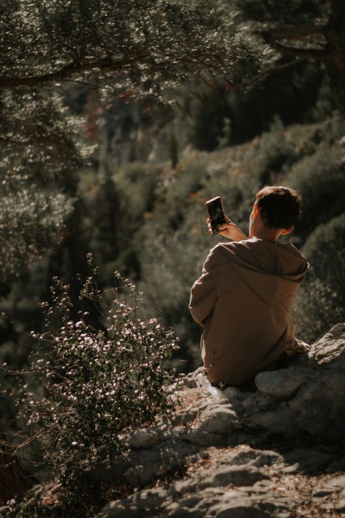 Free Person in a hoodie enjoying nature while using a smartphone on a rocky landscape. Stock Photo