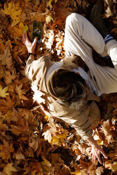 Top view of a person in autumn leaves holding a smartphone, capturing a serene fall moment.