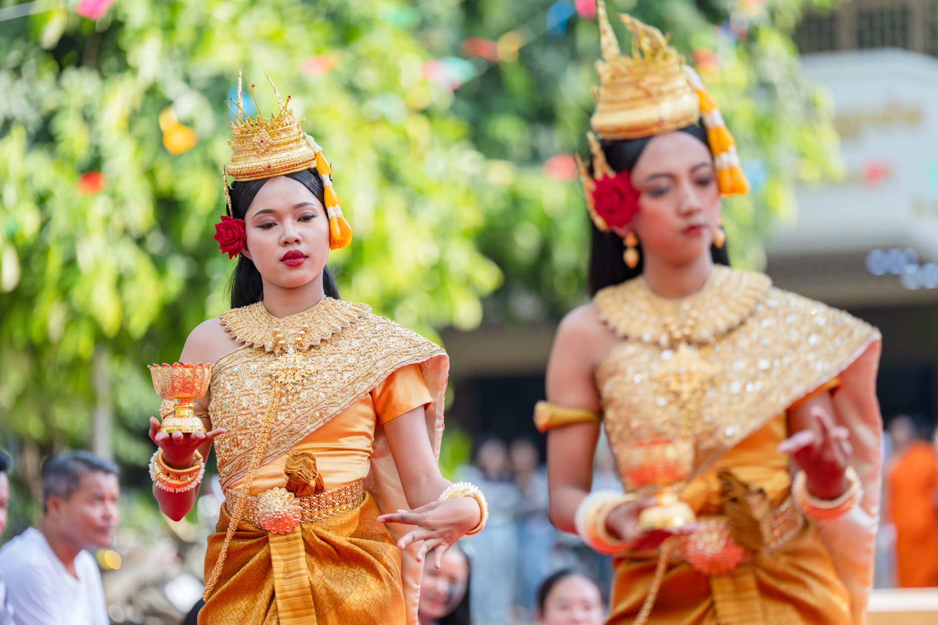 Women in ornate costumes perform a traditional Cambodian dance outdoors.