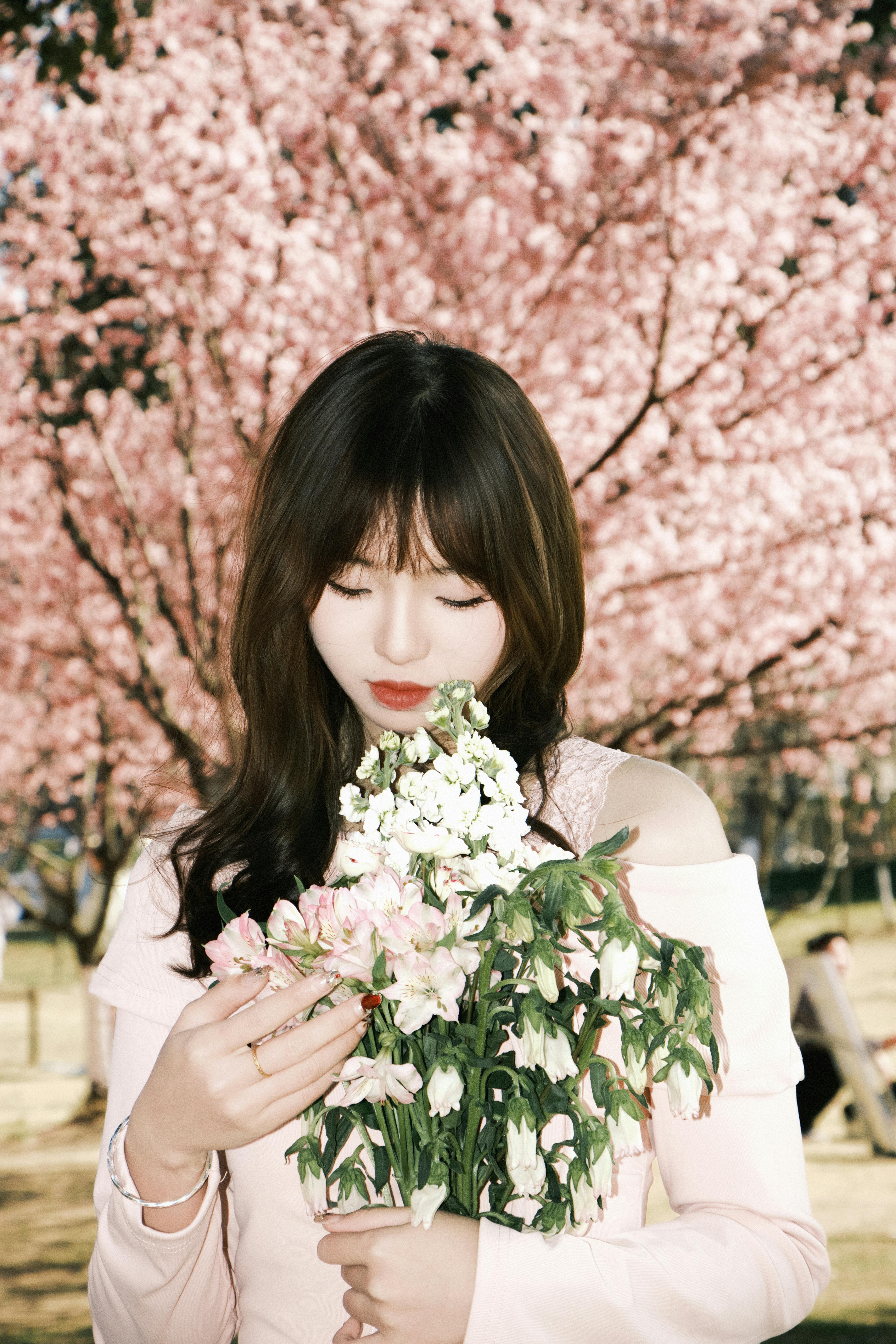 Young woman with a bouquet of flowers standing in a park with cherry blossoms in spring.