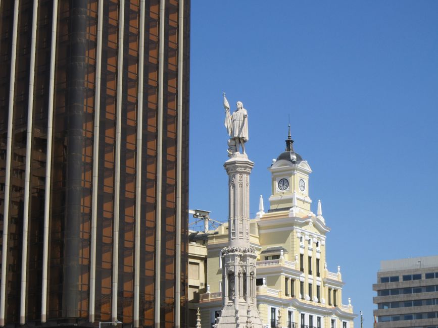 Un vibrante paisaje urbano de Madrid con edificios modernos y una estatua histórica bajo un cielo azul despejado.
