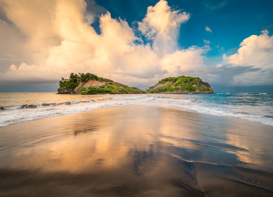 A stunning view of two lush islands off the coast of Sainte-Marie, captured at sunset with reflections on the sand.