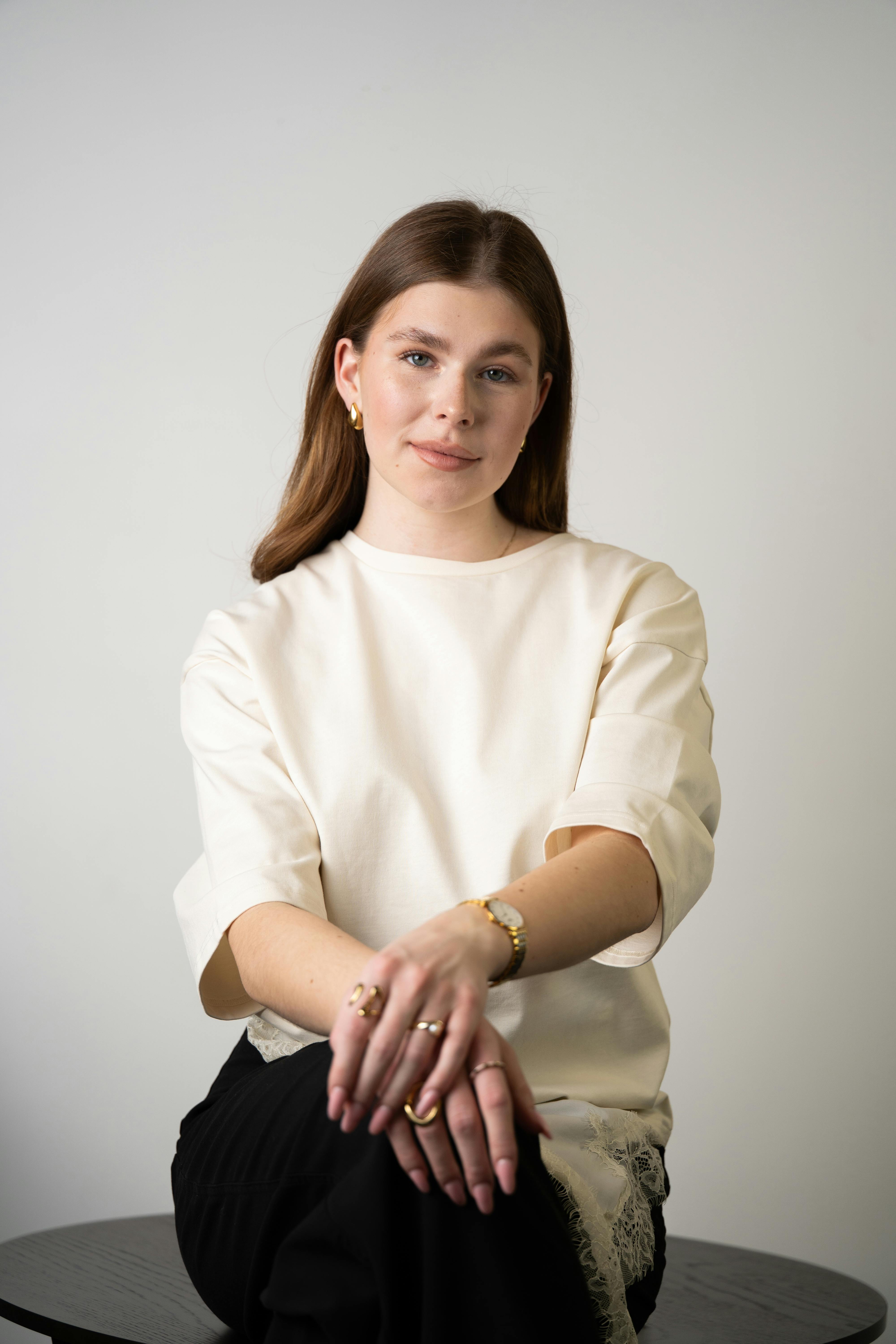 Stylish portrait of a woman in modern attire, sitting indoors with a neutral background.