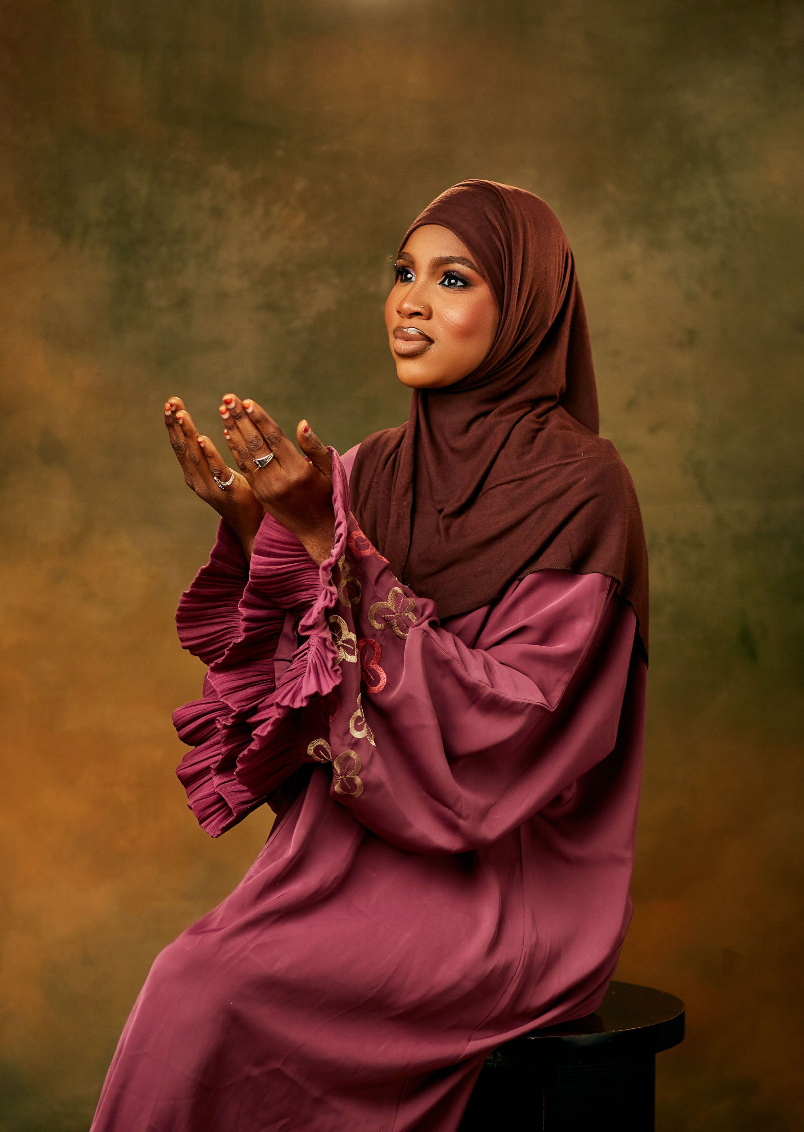 A woman wearing a hijab and traditional dress, praying with elegance.