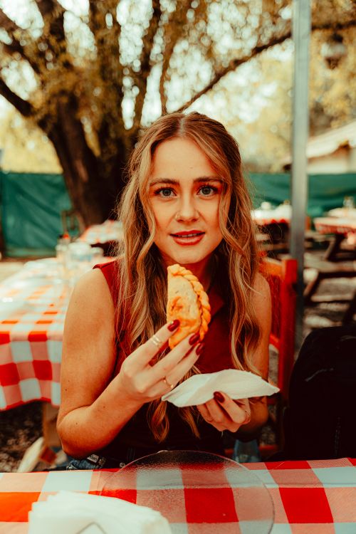 Free Young woman savoring a traditional empanada outdoors in Uribelarrea, Argentina. Stock Photo