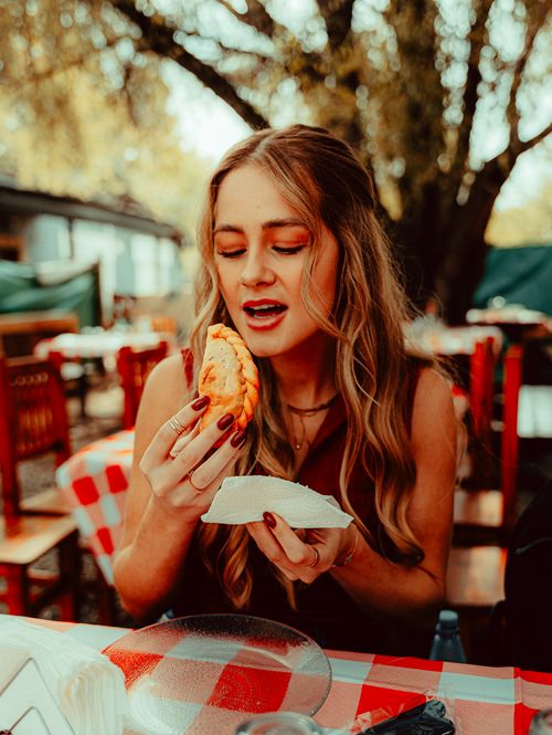 Free A young woman delighting in a traditional empanada at an outdoor cafe in Uribelarrea, Argentina. Stock Photo