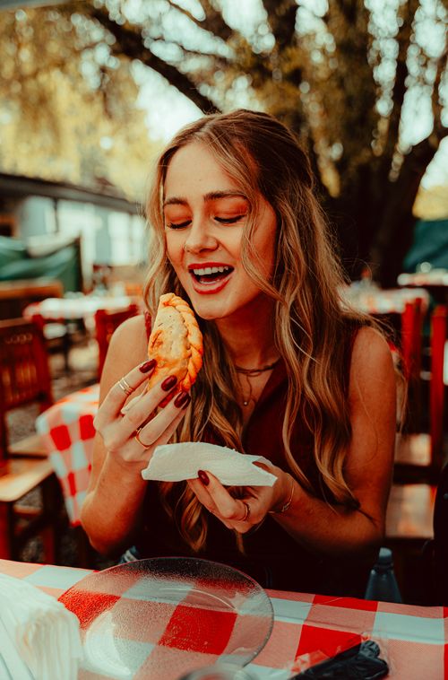 Free Woman smiling while enjoying a delicious empanada at an outdoor restaurant. Stock Photo
