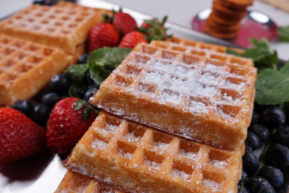 Appetizing close-up of golden waffles topped with powdered sugar and fresh berries, offering a delightful breakfast treat.