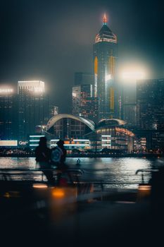 City skyline at night with towering skyscrapers, illuminated lights, and silhouettes by the water.