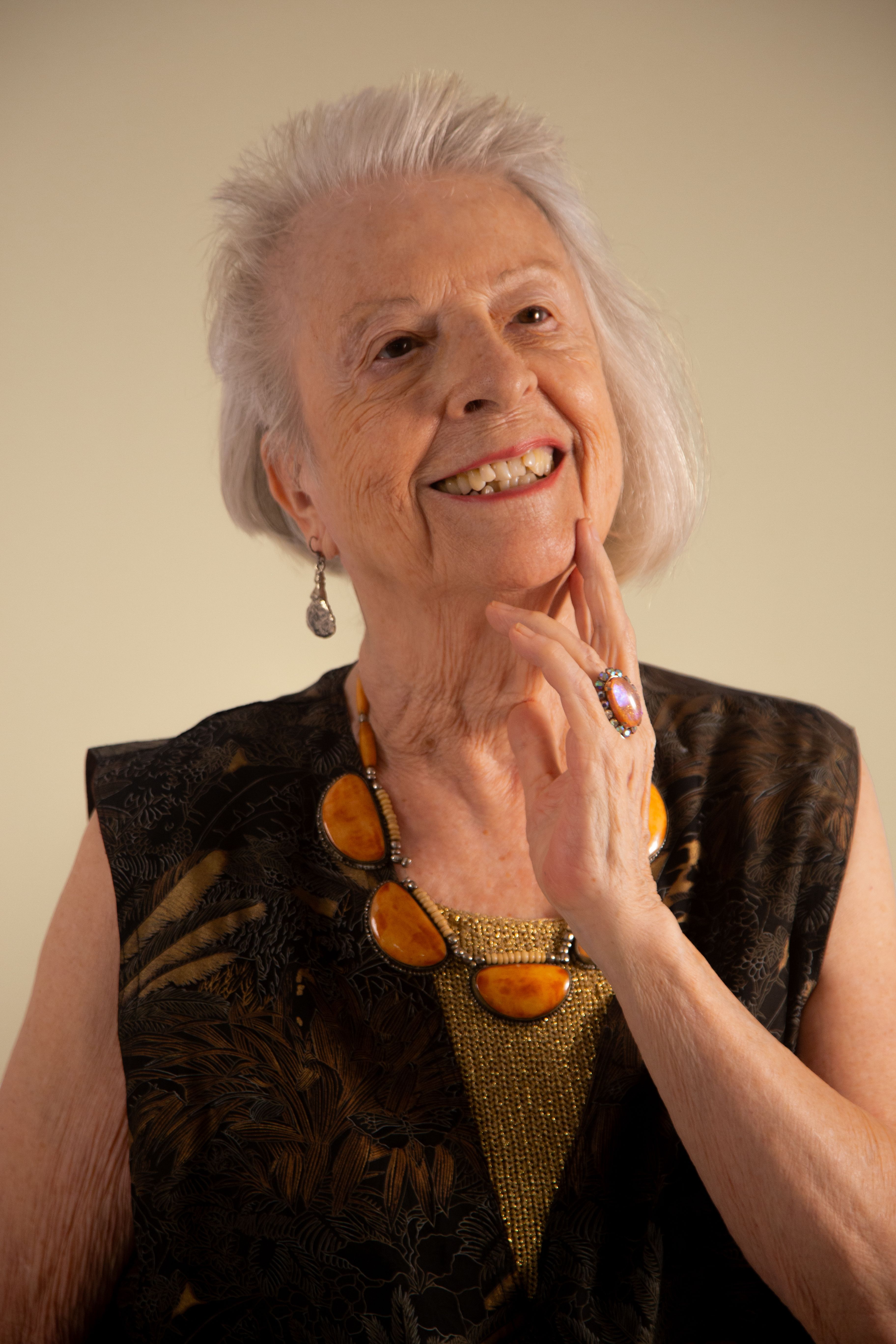 Smiling senior woman with stylish jewelry in elegant attire, showcasing grace and positivity.