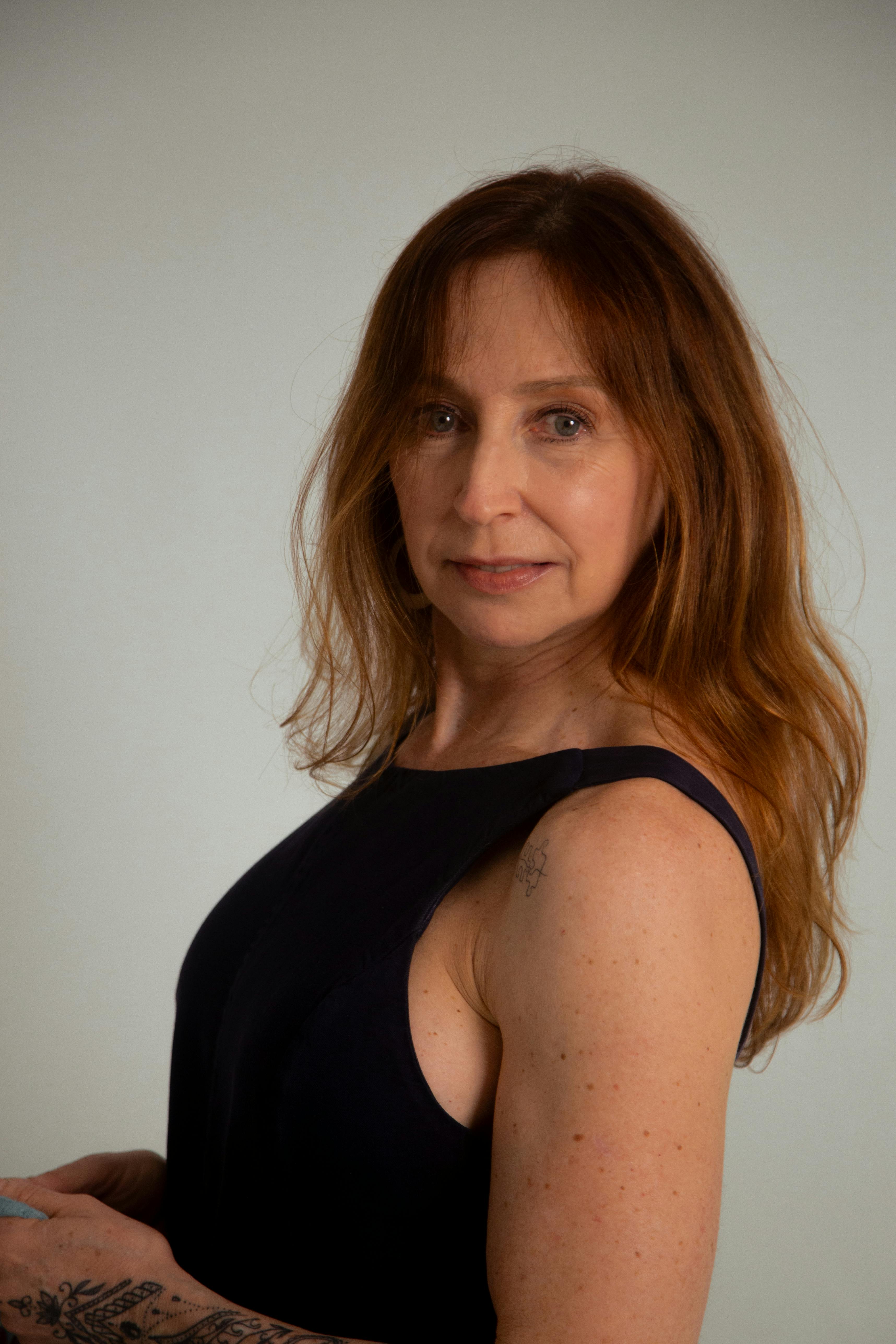 Elegant portrait of a woman with long brown hair in a sleeveless navy dress.