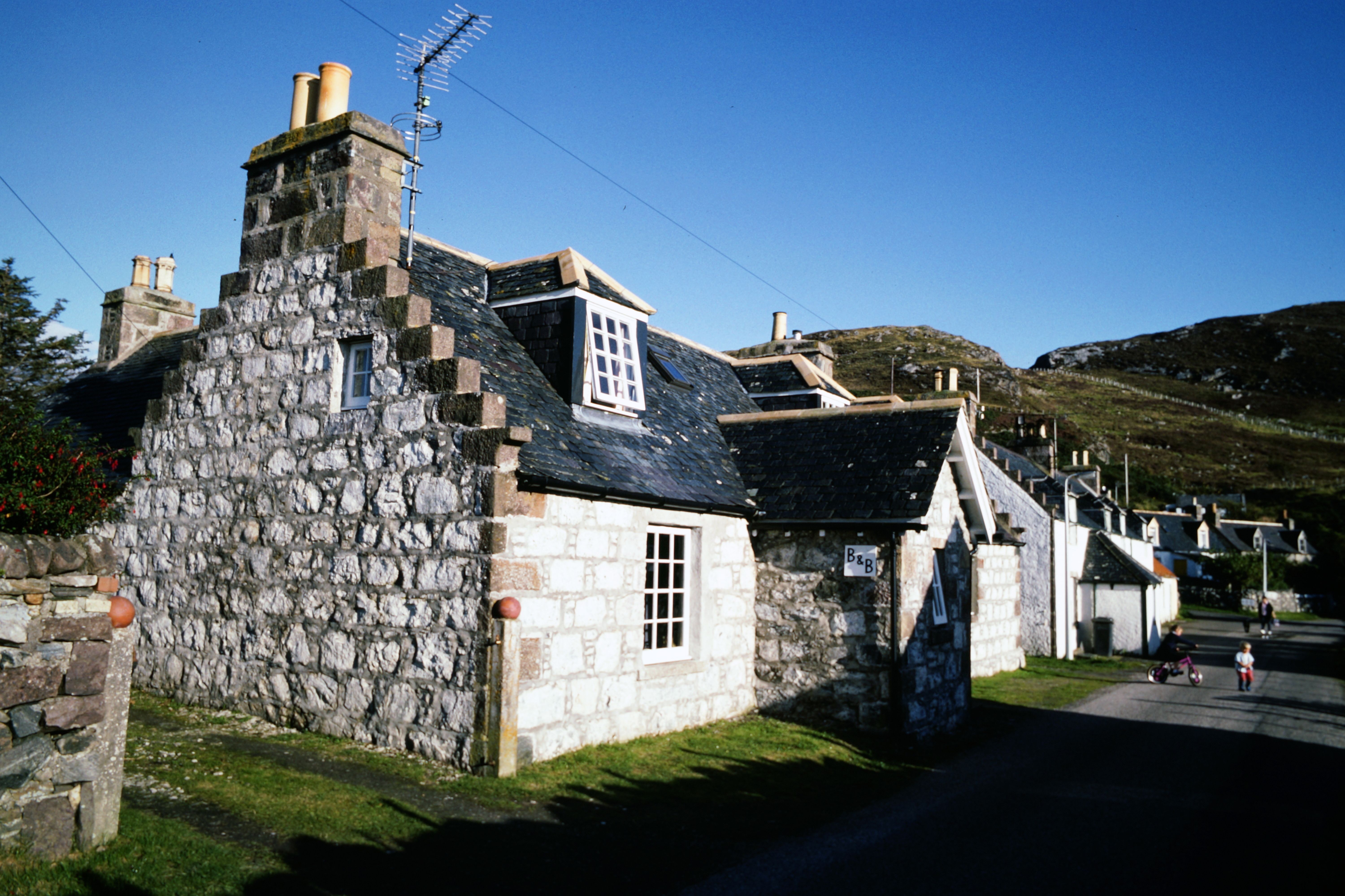 Traditional stone cottage basking in sunlight in the serene Scottish Highlands.