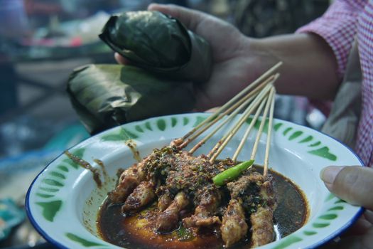 Street food satay skewers with spicy sauce, served on a rustic plate. Authentic culinary experience.