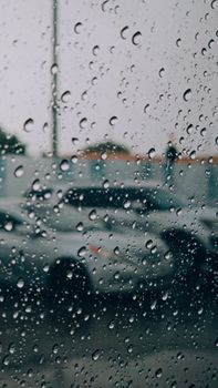 Blurred cars in a parking lot seen through a raindrop-covered window.