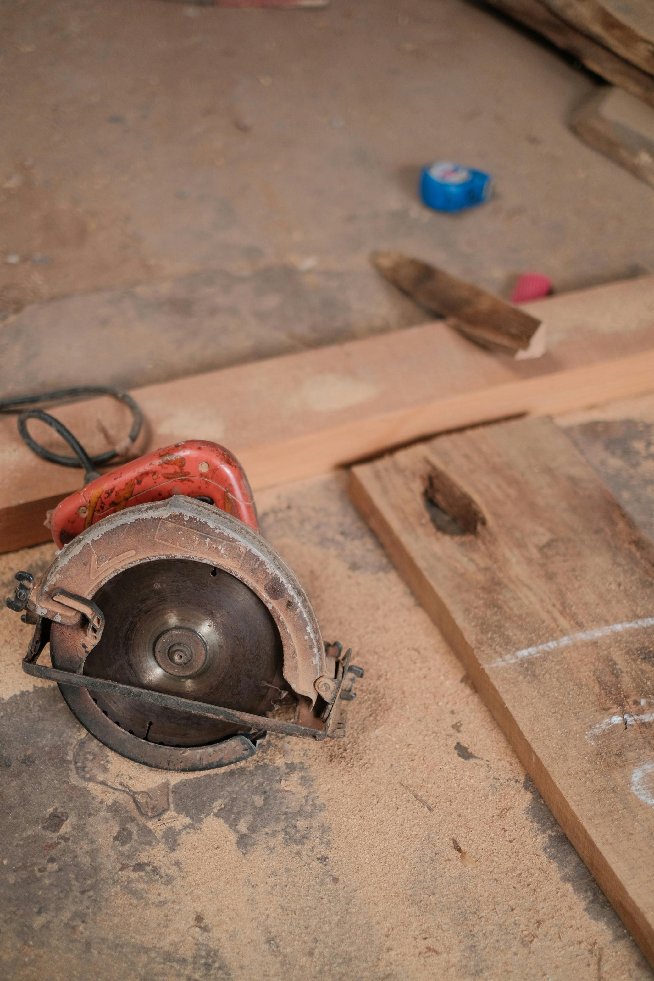 A circular saw on a dusty workshop floor, surrounded by wooden planks and tools.