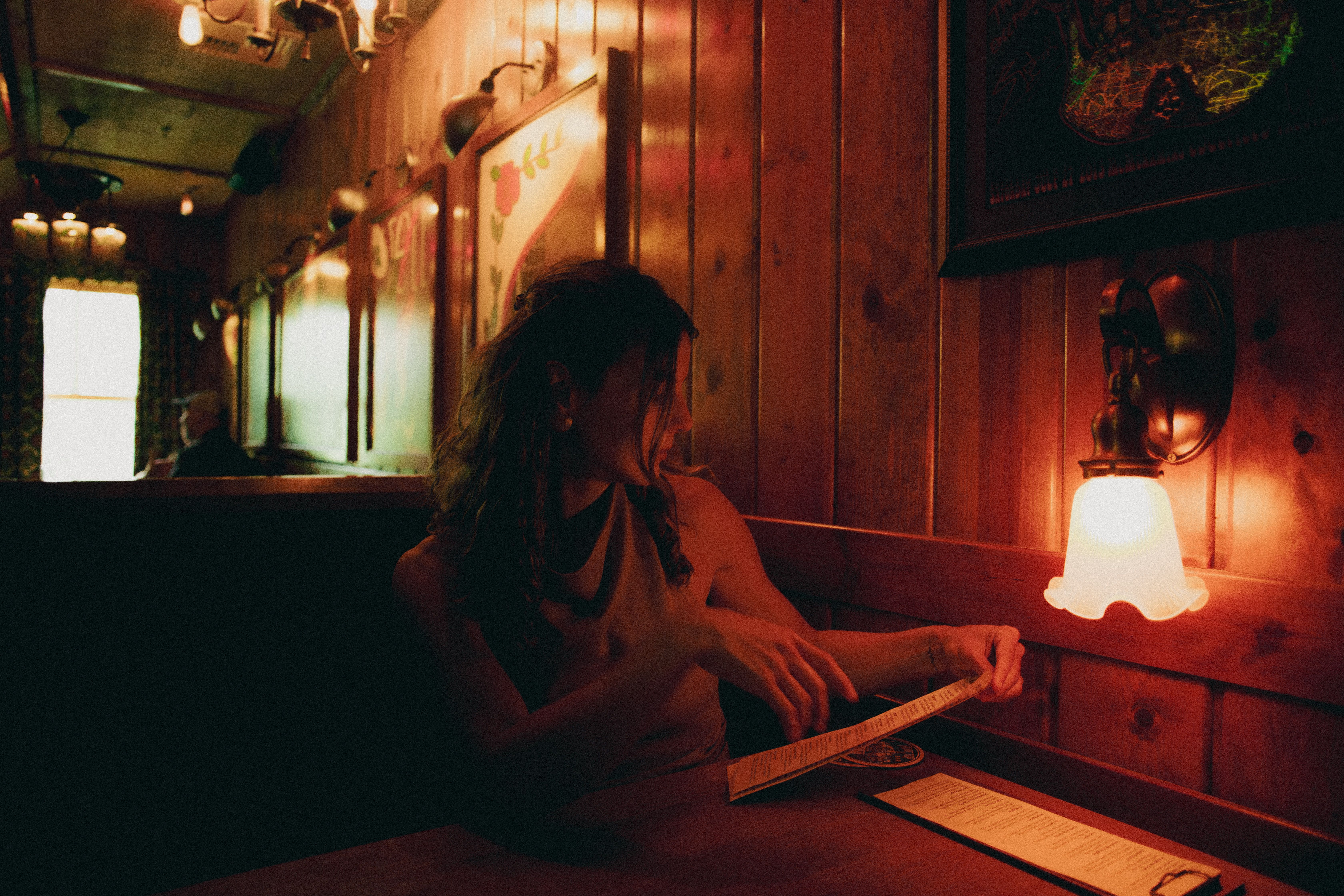 Woman in a dimly lit restaurant reviewing menu, warm and inviting.