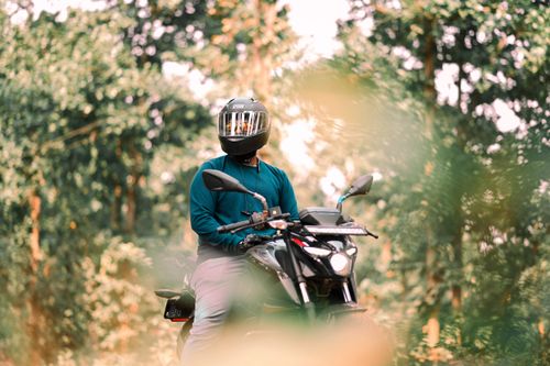 Free A motorcyclist wearing a helmet stands with a bike in a lush forest setting. Stock Photo