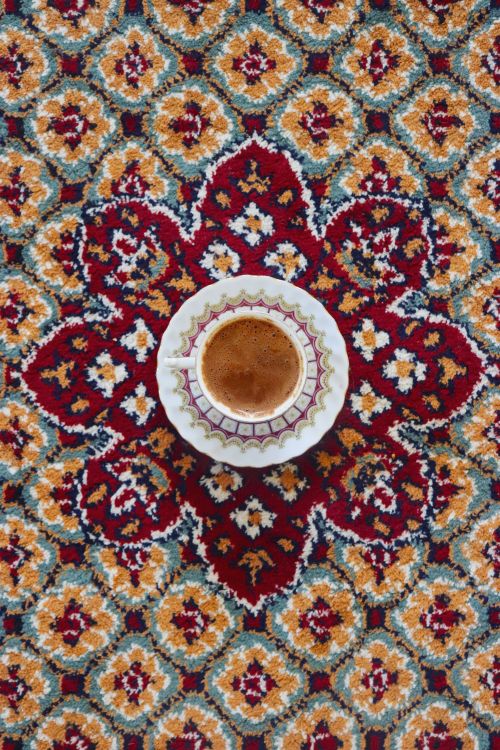 Free A cup of coffee resting on a beautifully patterned Persian carpet, showcasing rich colors and detailed designs. Stock Photo