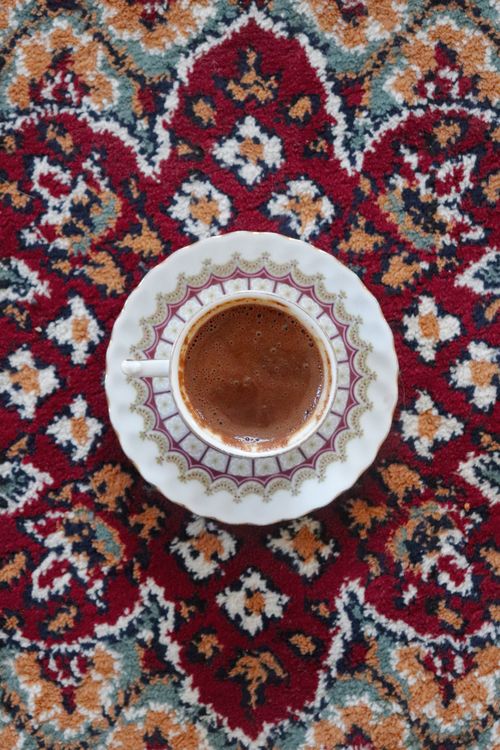 Free Overhead view of a beautifully patterned coffee cup on a colorful Persian rug, showcasing intricate design. Stock Photo