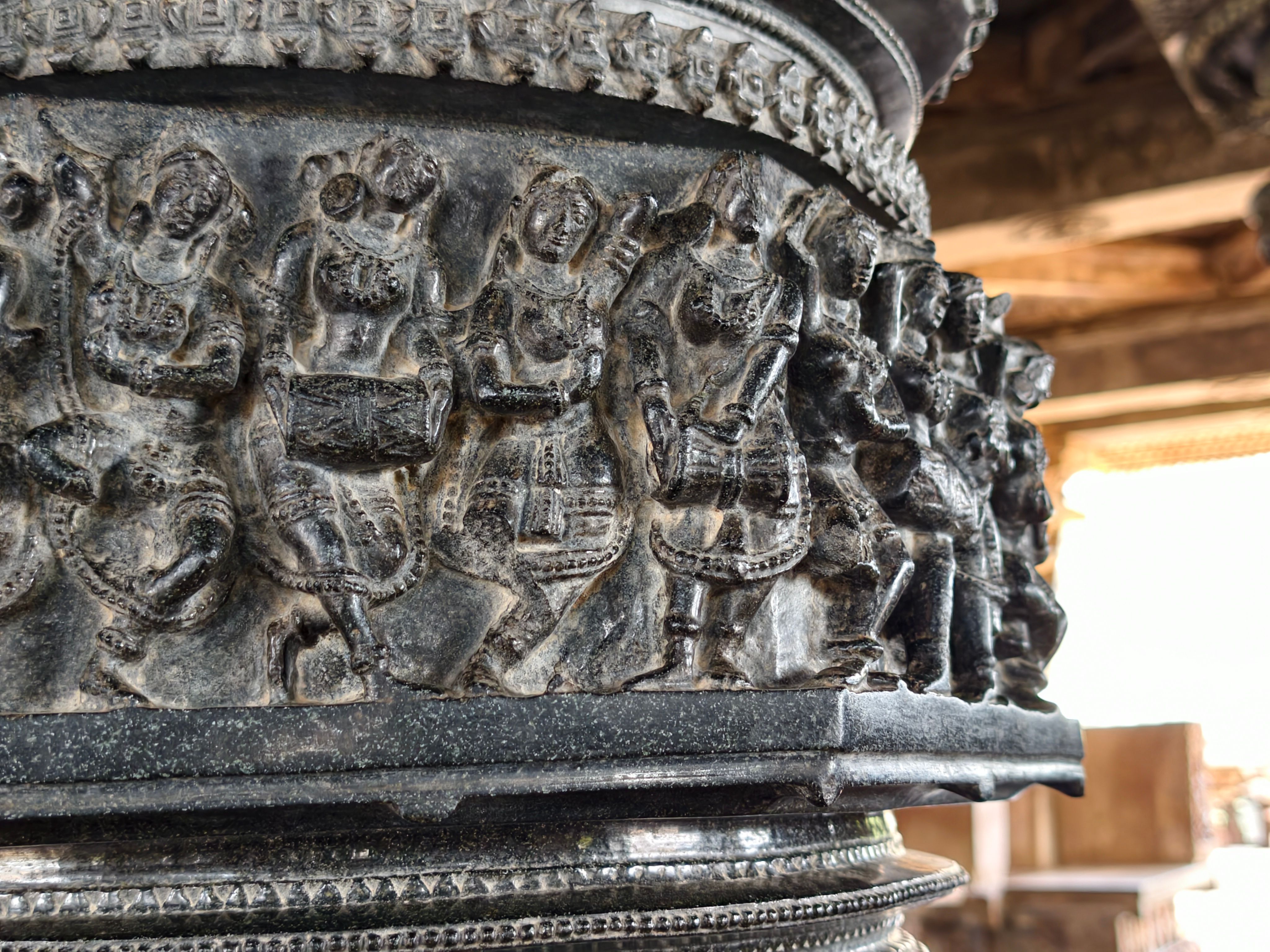 Detailed stone carvings depicting figures on an ancient pillar indoors.