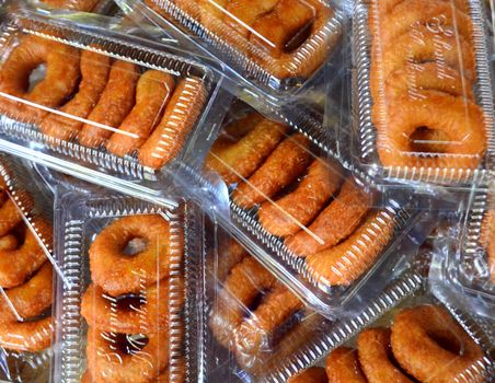 Close-up of Indonesian fried dough rings stacked in clear plastic trays, showcasing traditional snacks.