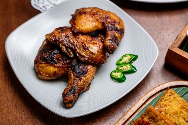 Authentic Indonesian grilled chicken served with fresh green chilies on a traditional plate.