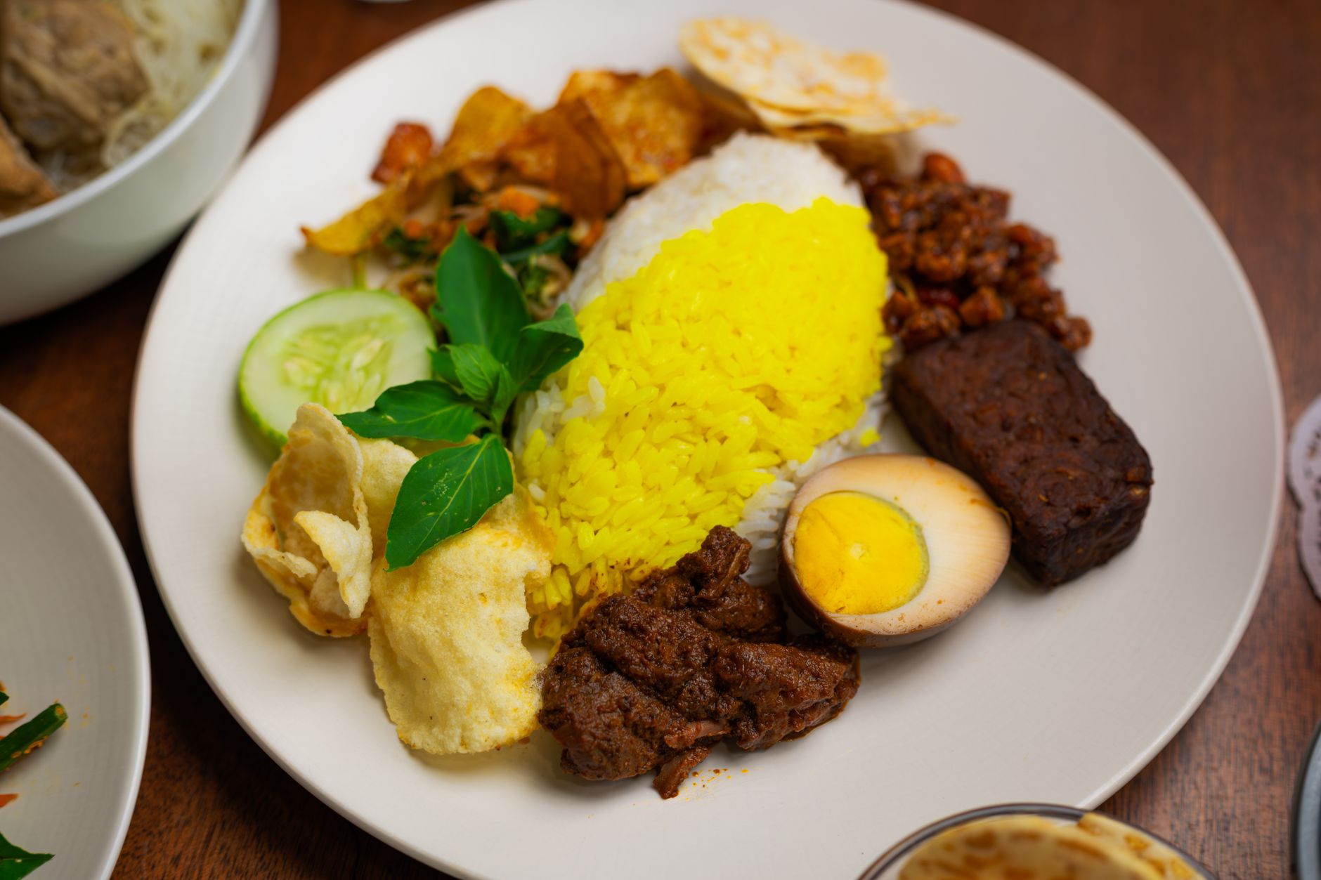 Colorful plate of traditional Indonesian Nasi Campur with yellow rice, grilled beef, egg, and sambal.