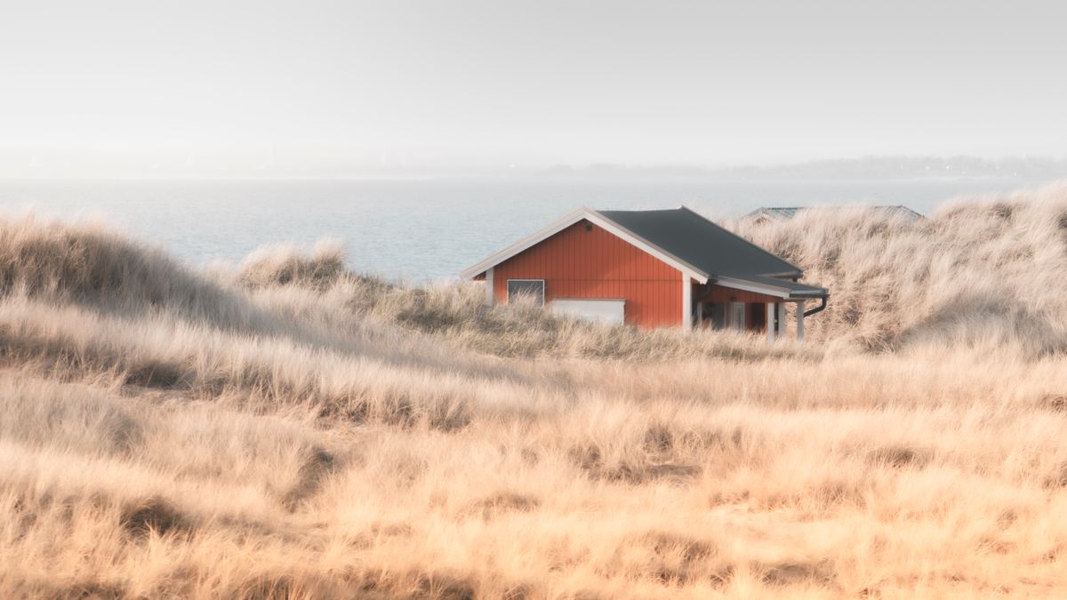 Red cottage near sandy coastal dunes; illustrative photo, not one of the named PEI properties