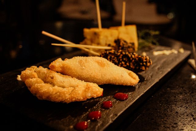 Delicious gourmet dish featuring fried empanadas and skewers on a dark serving platter.