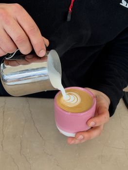 Barista pouring milk to create latte art in a pink cup at an İstanbul café.