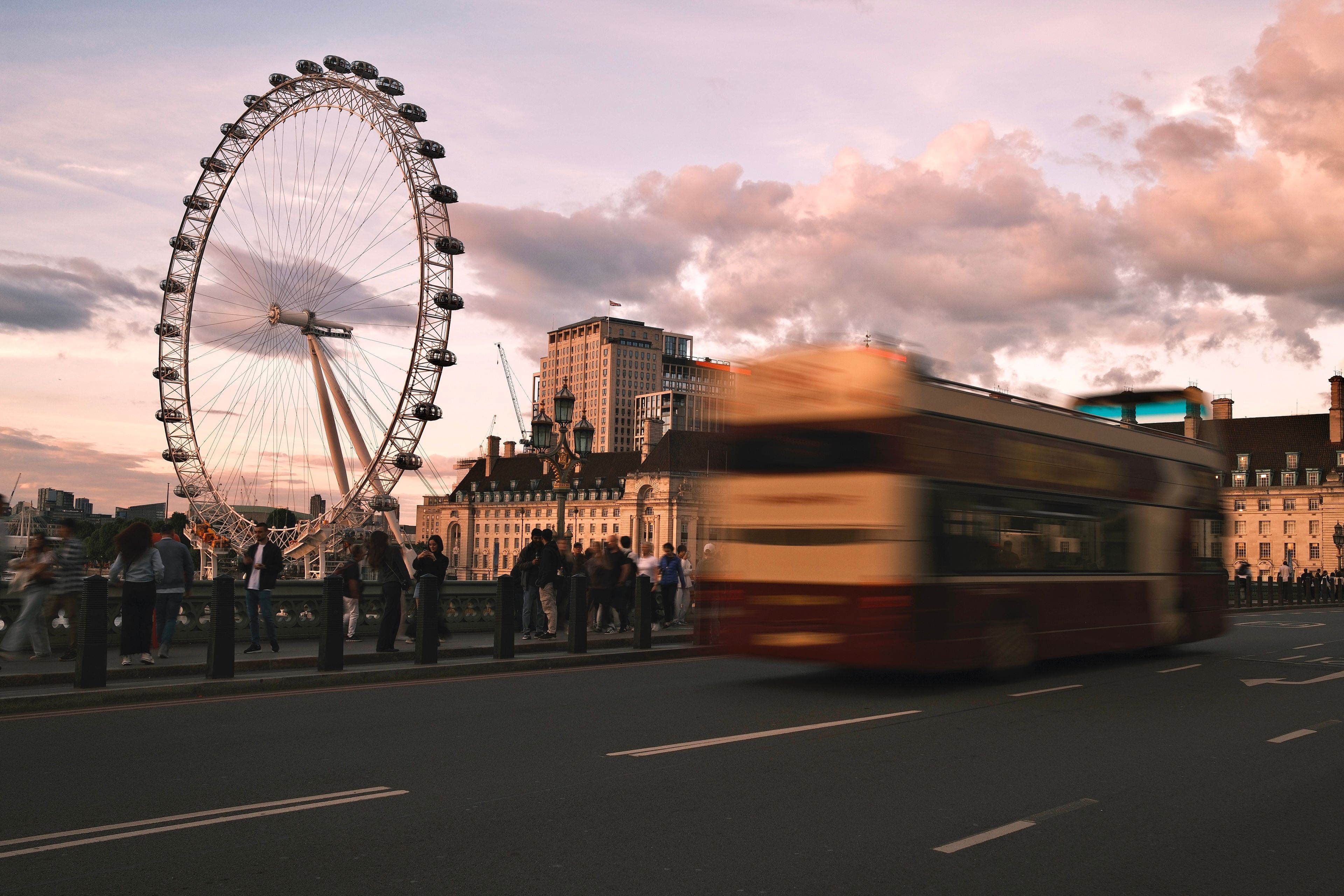 Blurred motion of a double-decker bus with the London Eye in the backdrop during sunset.