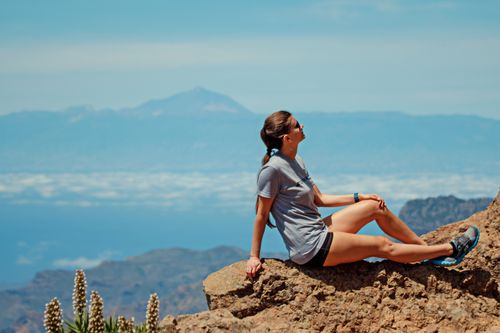 Free A woman relaxing on a rocky mountain with a scenic view under a blue sky. Stock Photo