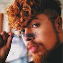 一位时尚红发男子的特写，他留着卷发，戴着独特的眼镜