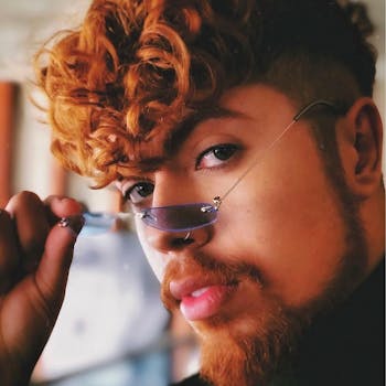 一位时尚红发男子的特写，他留着卷发，戴着独特的眼镜